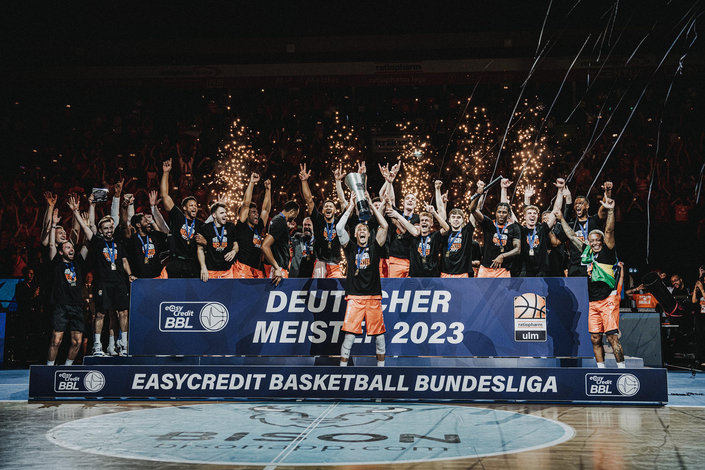 Um 22:34 Uhr stehen die Uhren still. Das Horn erklingt, die Saison 2022/2023 in der easyCredit BBL ist beendet. In der Arena brandet ohrenbetäubender Jubel auf. Das Team von ratiopharm ulm hat soeben die erste Deutsche Meisterschaft der Vereinsgeschichte gewonnen. im vierten, einem abermals umkämpften Spiel einer packenden Serie gegen die Telekom Baskets Bonn setzen sch die Schwaben mit 74:70 durch, wobei ein 18:0-Lauf zu Beginn des letzten Viertels die Weichen auf Sieg stellt. Mit Yago dos Santos (25 Punkte, 8 Assists) wird erstmals ein Brasilianer zum wertvollsten Spieler der Finals gekürt.