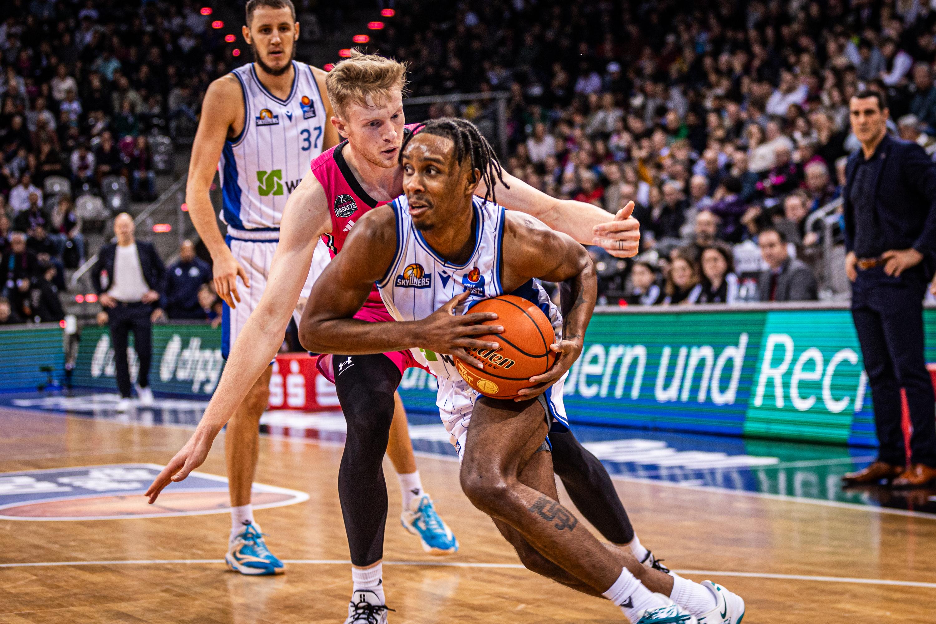 Die Telekom Baskets Bonn haben einen vollen Kader und einen ausverkauften Telekom Dome (6.000 Zuschauer) im Rücken. Die SKYLINERS aus Frankfurt hingegen sind ersatzgeschwächt, aber treten im Rheinland mit Leidenschaft und Willen auf. Und einem Malik Parsons, der mit 22 Zählern zum bestimmenden Akteur wird. So wie die lange Garde der Gäste, die das Rebound-Duell klar für sich entscheiden (49:39) und so letztlich das 77:70 sichern.